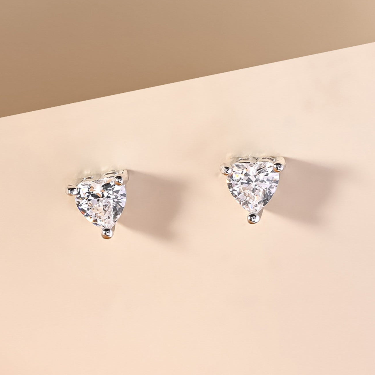 Heart-shaped diamond earrings on a beige background